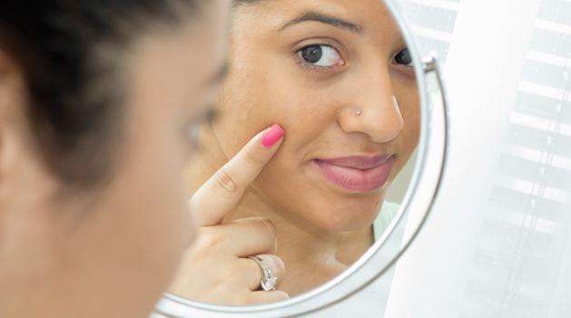 Femme qui regarde sa peau dans un miroir