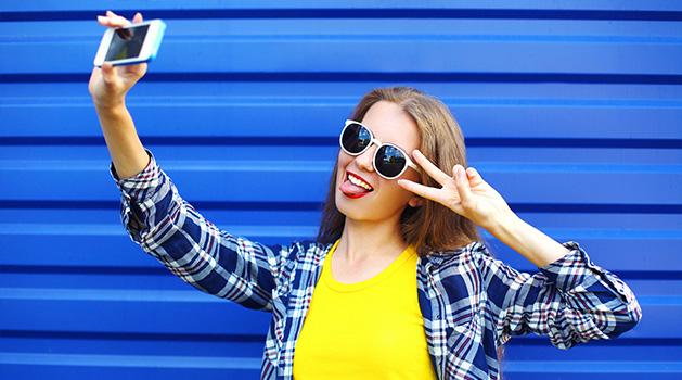 girl wearing sunglasses taking a selfie with her phone